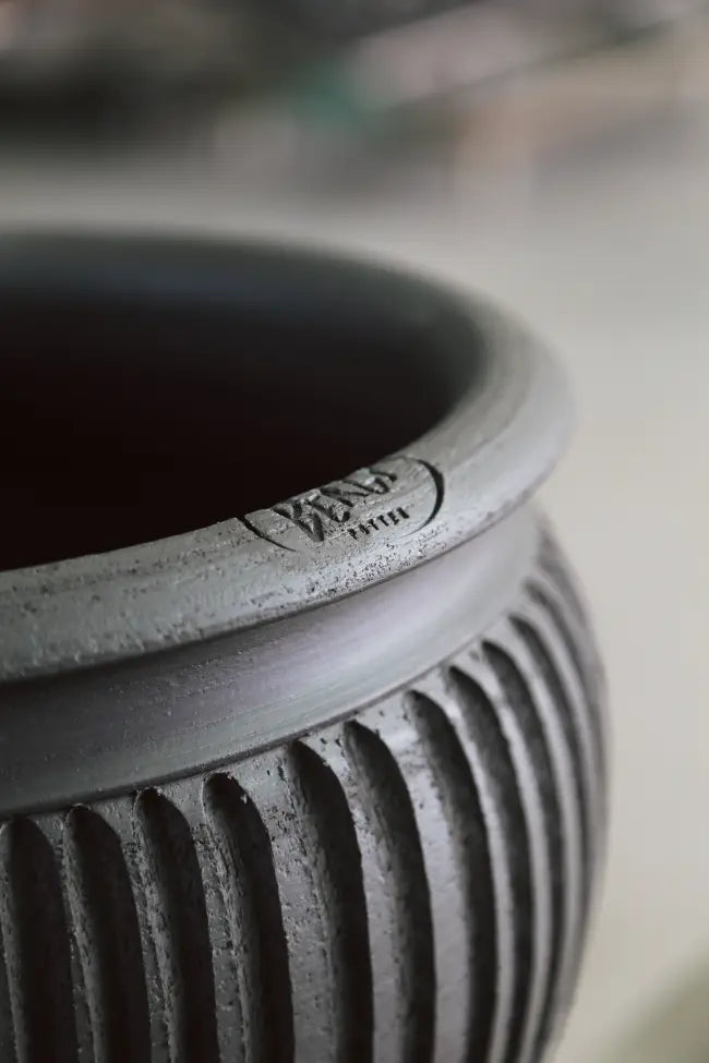 Close-up of a textured work-in-progress black Bergs Potter pot with a brand logo on a blurred background