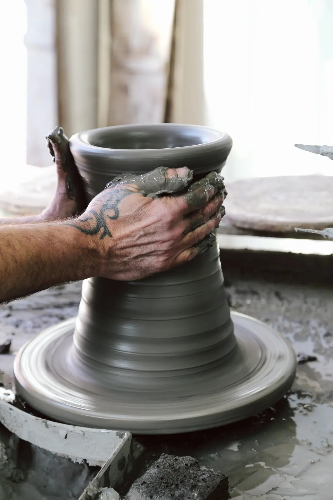 Person shaping a clay pot on a pottery wheel